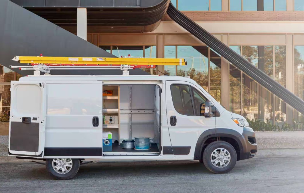 Ram ProMaster cargo van with its side door open showing interior shelving and a ladder rack
